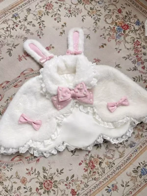 White fuzzy bunny ear plush lolita cape with pink bows and delicate lace hem, flat lay display on vintage floral carpet