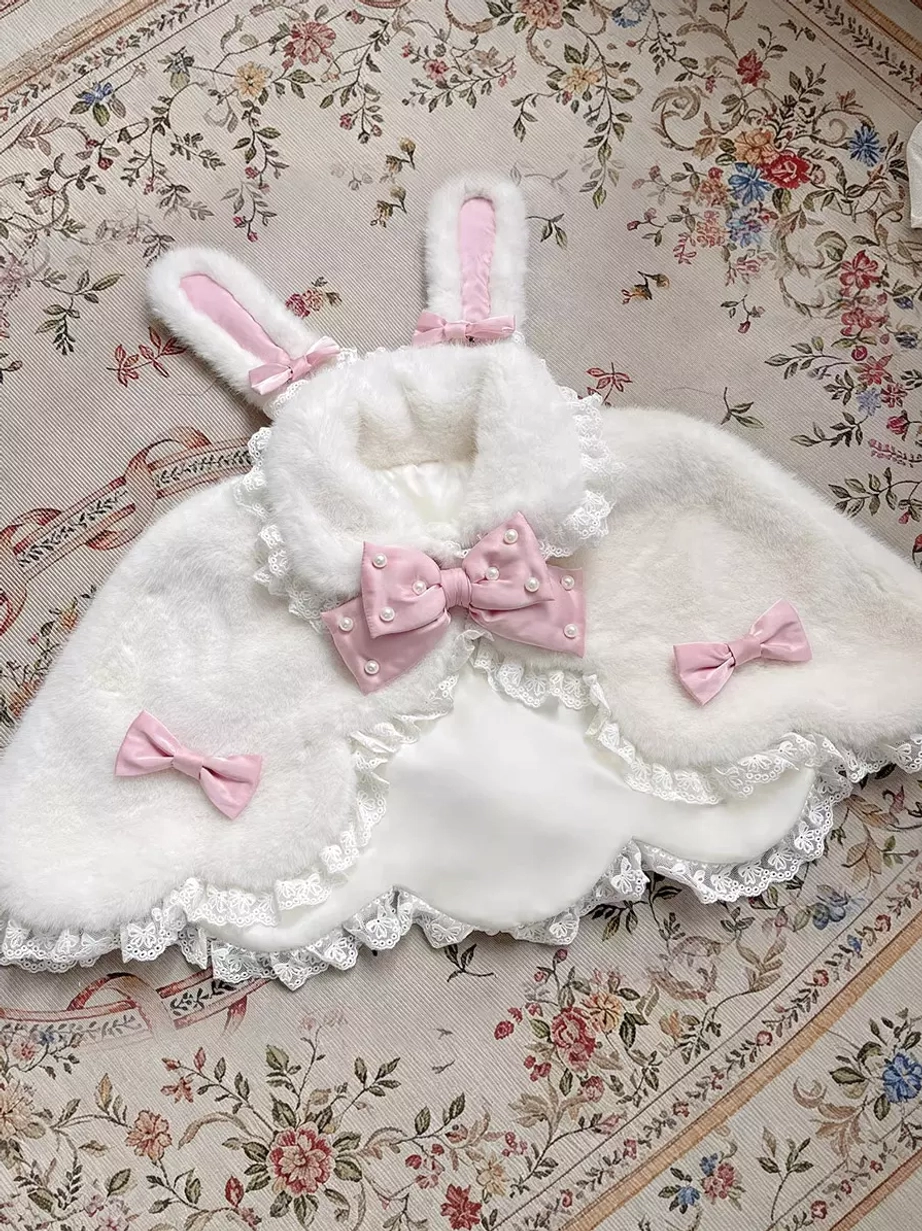 White fuzzy bunny ear plush lolita cape with pink bows and delicate lace hem, flat lay display on vintage floral carpet