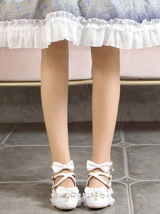 White cross-strap lolita pumps with ruffled toe cap and bow decorations displayed on model wearing traditional ruffled lolita dress, showing full front leg view of ankle strap configuration and delicate aesthetic details