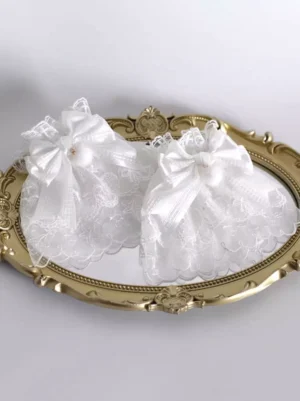Pair of white embroidered sheer lace fingerless gloves with satin bows and pom-pom accents arranged symmetrically on ornate gold tray, sweet lolita rococo style accessories flat lay