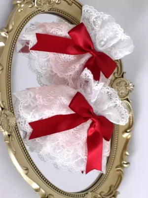 white floral lace wrist cuffs with red satin bows and pink inner lining displayed on vintage gold carved mirror rococo style sweet lolita accessories