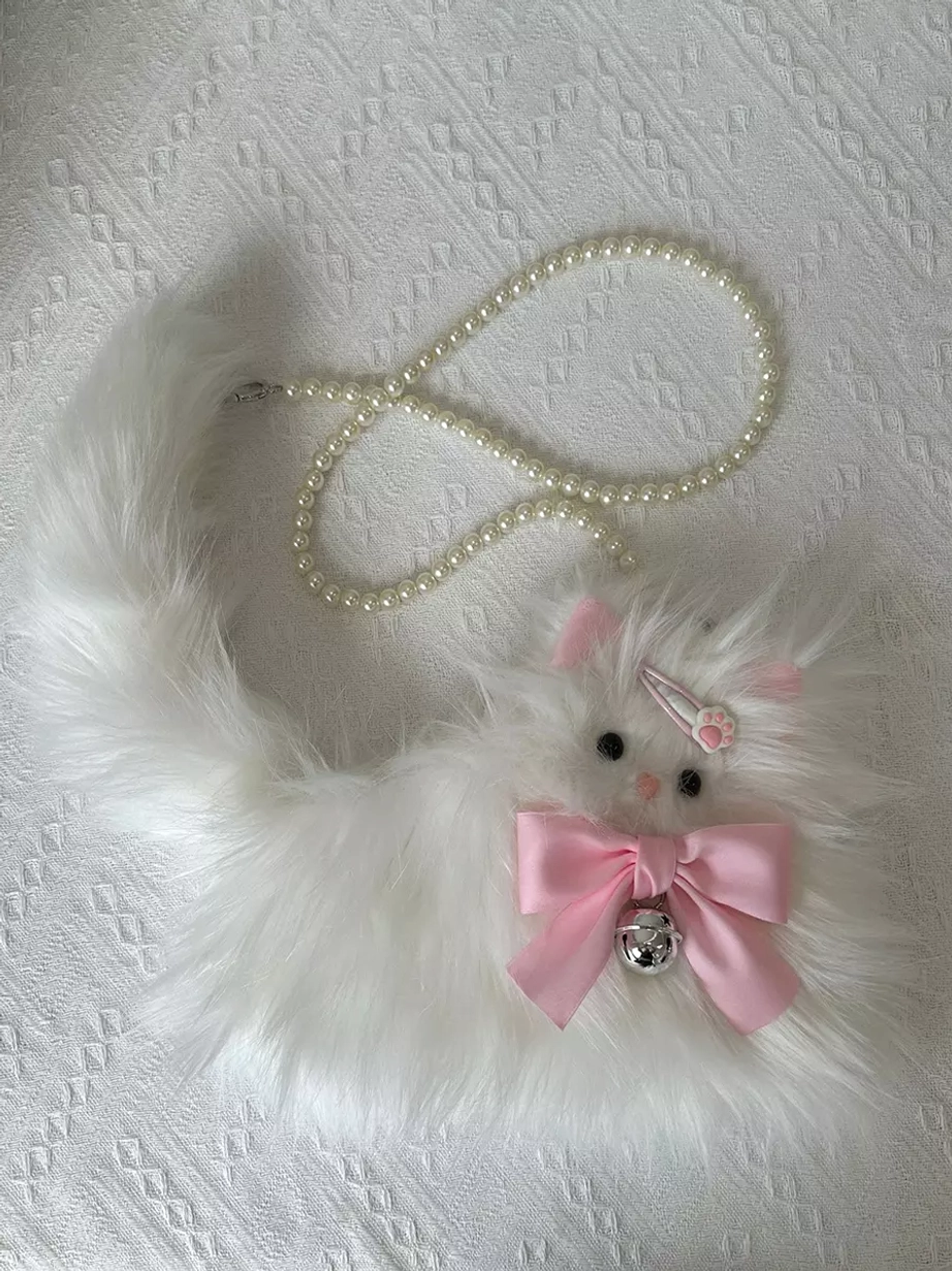 Plush white cat crossbody bag on textured white fabric background displaying faux fur texture, pink bow embellishment with silver bell, and pearl chain strap