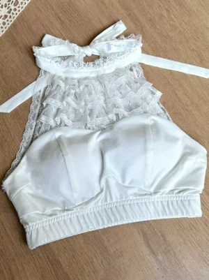 Sleeveless white halter lingerie crop top with layered sheer lace front panel solid padded bust and self-tie halter bow top view