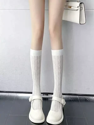White heart hollow knit lolita knee-high socks front view on female legs wearing white Mary Jane shoes indoor preppy style stockings