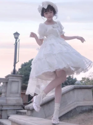 White Hime Lolita dress with layered tulle skirt and chest bow, worn with hair bow accessory on outdoor stone stairway with model in three-quarter dynamic pose