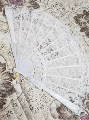 White lace folding hand fan with gold carved plastic frame and decorative hanging ring poly-cotton blend lace accessory flat lay overhead shot