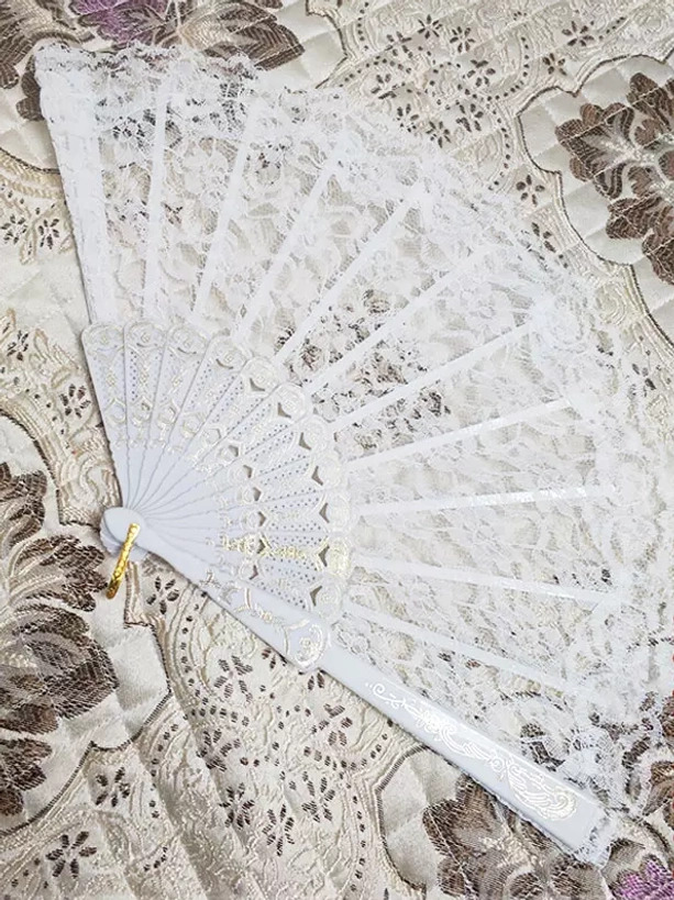 White lace folding hand fan with gold carved plastic frame and decorative hanging ring poly-cotton blend lace accessory flat lay overhead shot