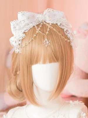 White lace lolita head bow with gold decorative chains and crystal snowflake pendant headdress accessory, showcased on mannequin with light brown wig against pink background, perfect for sweet lolita fashion coordinates and cosplay events