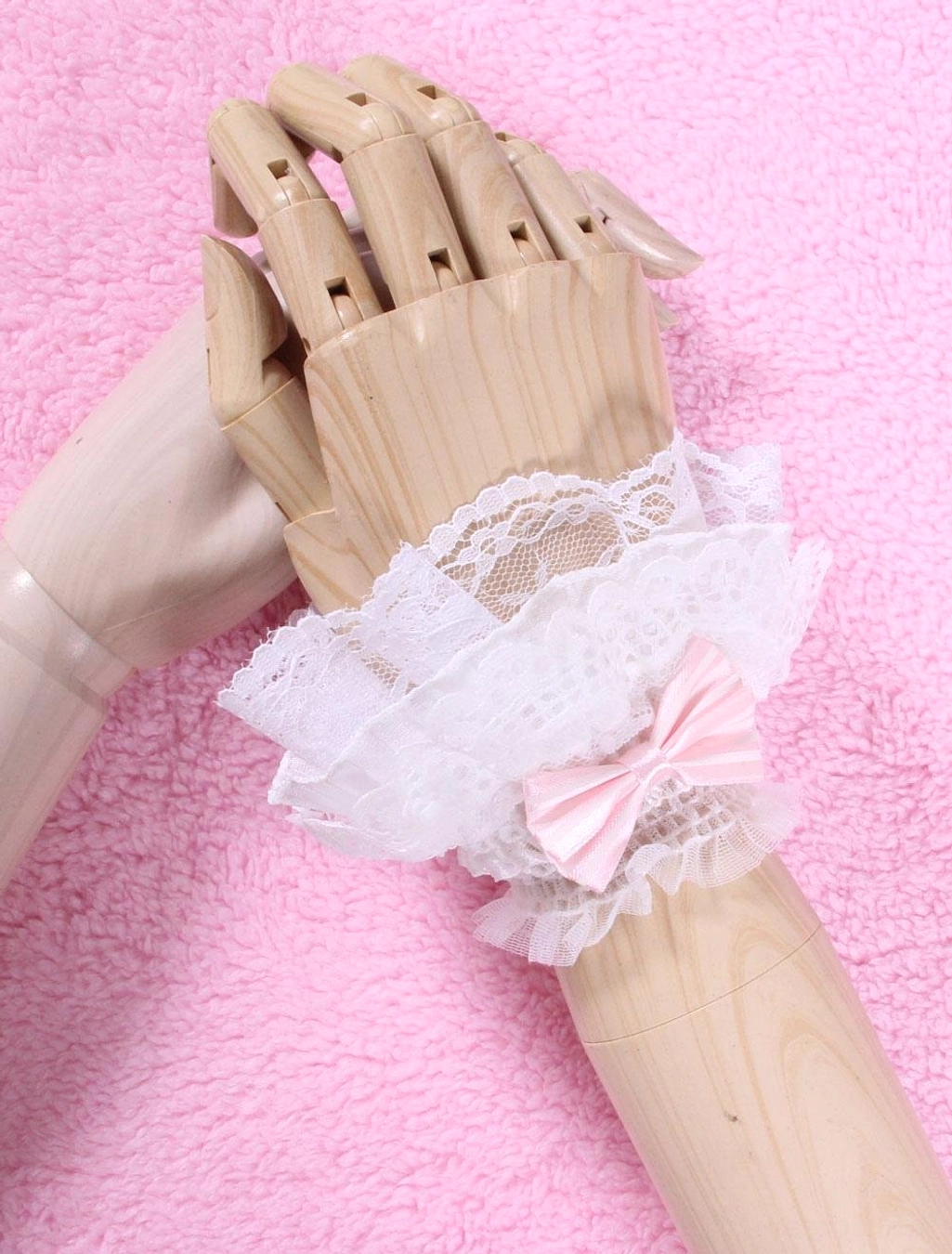 white lace lolita wrist cuffs with pink satin bow overhead front view on wooden mannequin hands