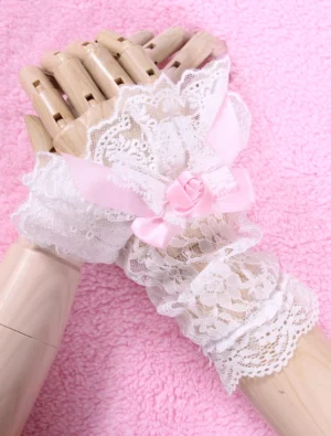 White lace Lolita wrist cuffs overhead view with pink satin bow and rose detail on wooden mannequin hand against pink plush background