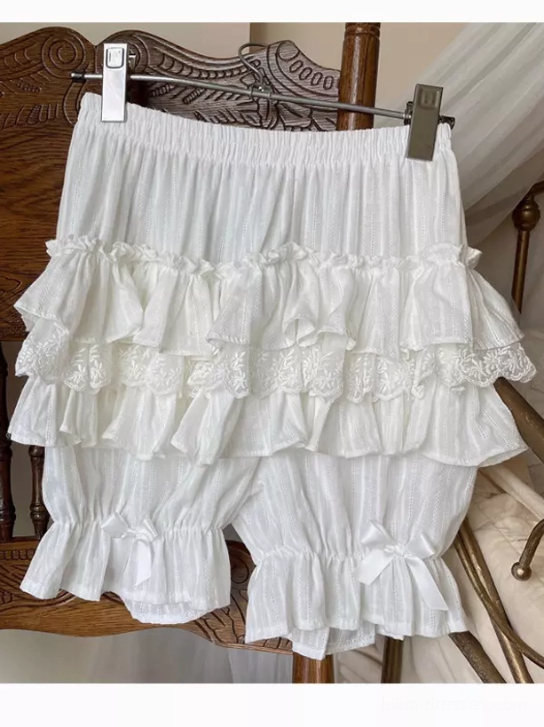 White lolita bloomers flat lay with multiple layered ruffles elastic waist bowknot on leg openings vintage wooden furniture background
