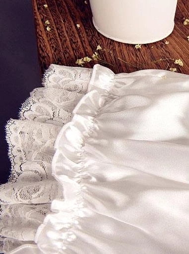 White lolita bloomers side detail view showing layered lace ruffle trim, white satin fabric, and elaborate lace hem construction on decorated wooden table surface