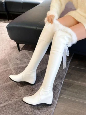 white over-the-knee lolita boots with faux fur collar and lace ribbon tassel worn on model in beige knitwear indoor setting