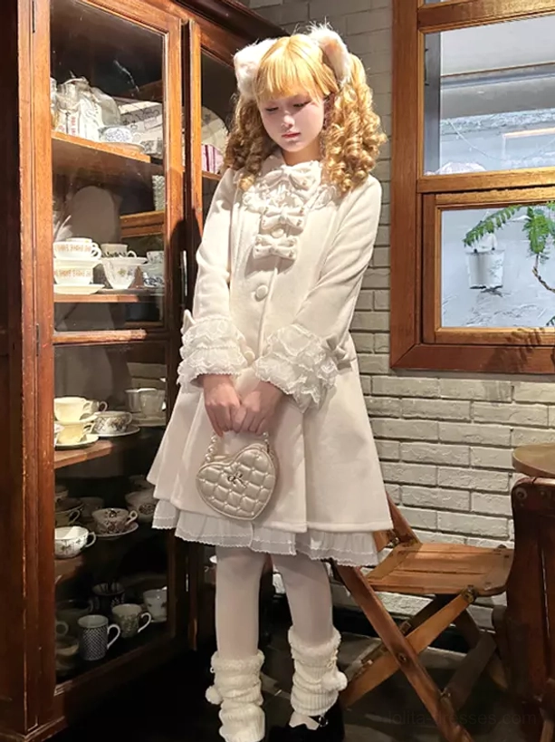 White sweet lolita coat full body front view worn with cat ear hair clips in vintage cafe setting showing ruffled cuffs and bow neckline