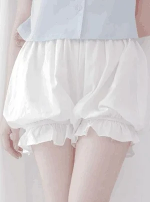 White lolita cotton bloomer shorts with ruffled elastic leg cuffs and gathered waist, paired with light blue cropped button shirt, front view showing voluminous silhouette from waist to mid-thigh