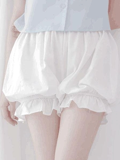 White lolita cotton bloomer shorts with ruffled elastic leg cuffs and gathered waist, paired with light blue cropped button shirt, front view showing voluminous silhouette from waist to mid-thigh