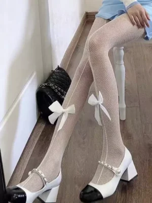 White cream lolita fishnet tights with bow ankle embellishment paired with blue skirt on wooden floor, displaying fine mesh weave and decorative bow details in side profile