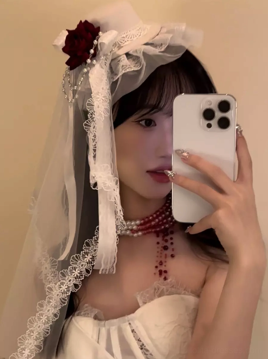 White Lolita headpiece featuring lace veil, red rose decoration, and beaded necklace in front half-face selfie view on model in white strapless top