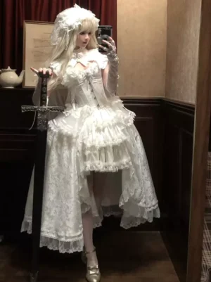 White fairy Lolita dress side view showing layered ruffles and high-low hem, paired with gold buckle heels and dramatic styling