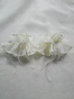 Pair of white lolita ruffled arm oversleeves flat lay featuring sheer organza construction, delicate lace-trimmed hanging ribbons, and centered bow accents displayed on plain white fabric background