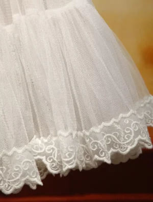 Close-up detail of white Lolita petticoat hem showing embroidered scroll pattern lace trim, ruffled tulle layers, and sheer organza fabric construction highlighting craftsmanship