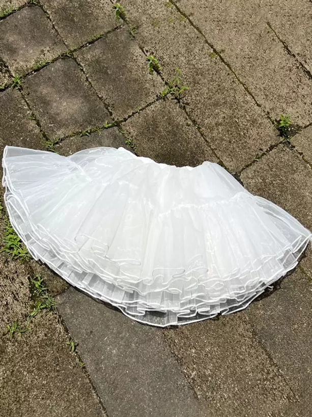 White lolita petticoat top-down overhead flat lay view on stone pavement showing multi-layer ruffled tulle hem and full underskirt dimensions
