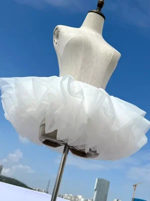 White ultra-puffy Lolita petticoat crinoline skirt with 6-layer soft tulle, front three-quarter view on mannequin displaying full rounded silhouette against urban sky backdrop