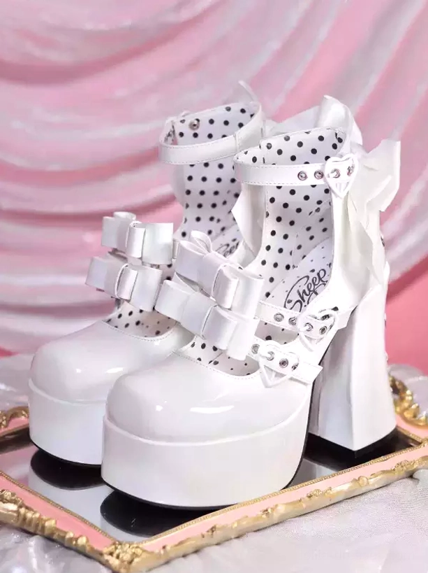 White lolita platform pumps with polka dot lining, dual front bows, and large back bow displayed on gold tray against pink satin backdrop
