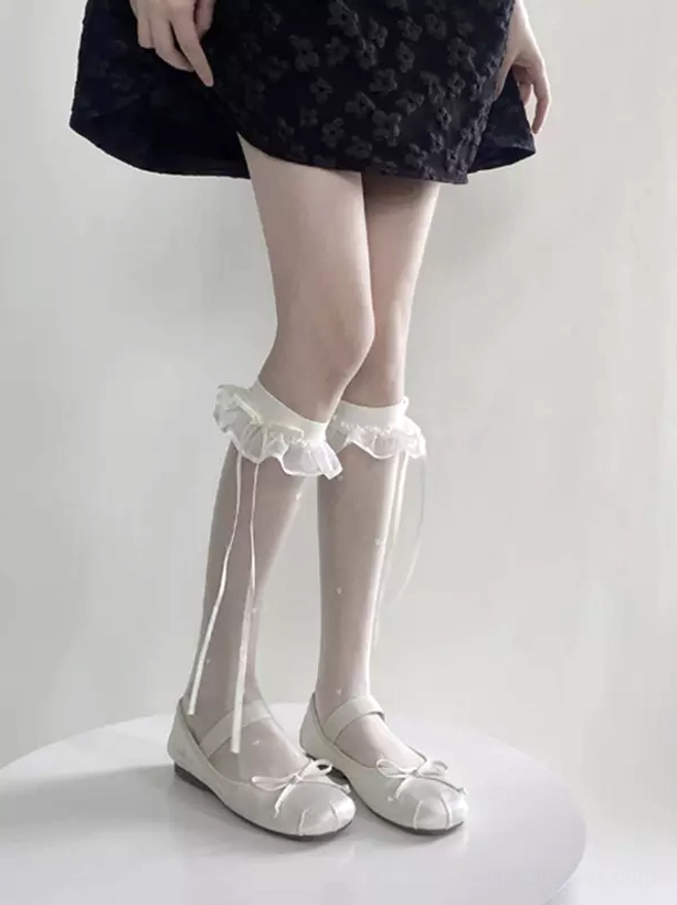 White ruffled ribbon calf stockings displaying sheer fabric construction, architectural ruffled cuff, and long satin ribbon details, side view of standing model in floral dress