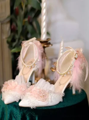 White lolita stiletto pumps with pink flowers and pearl ankle strap, overhead close-up view on vintage green velvet background, showcasing feather trim details and pointed toe design