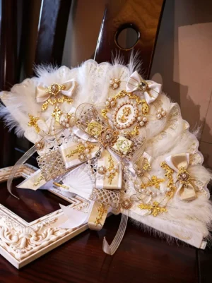 White ostrich feather folding fan with gold and ivory trim, pearl embellishments, and delicate lace bow detail, displayed on wooden surface with vintage frame, perfect Lolita wedding accessory and fashion prop