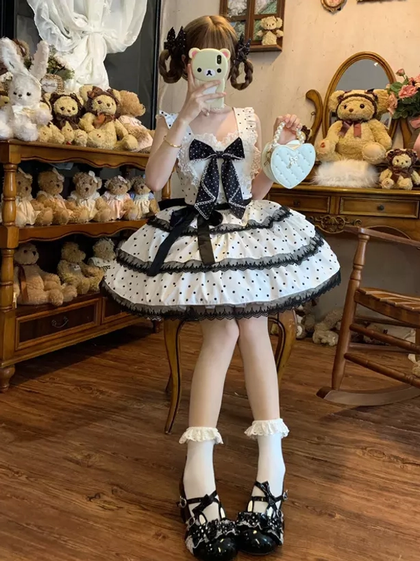 White polka dot sweet lolita jumper skirt dress full body front view with black bow detail and layered lace ruffle socks