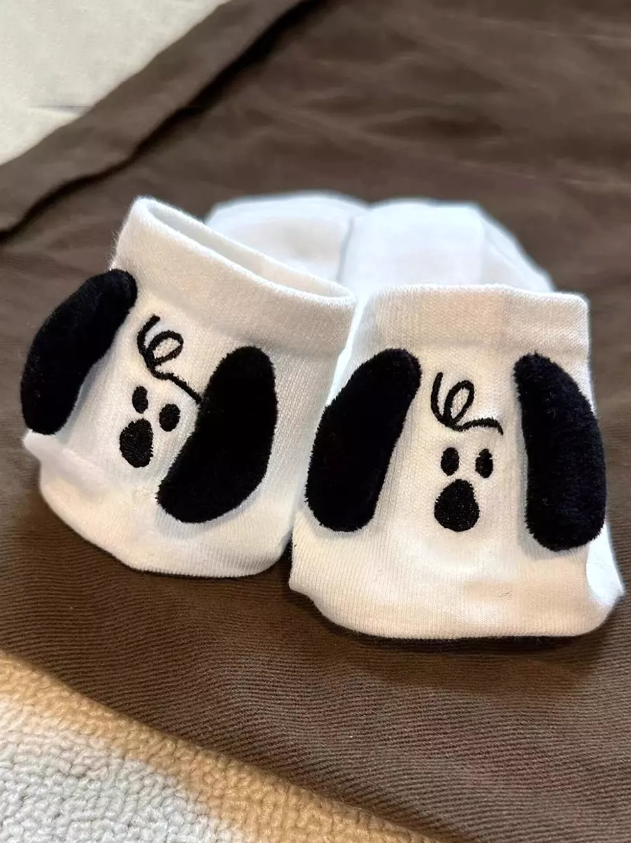 Pair of white 3D puppy plush lolita socks flat lay on brown fabric background showing matching embroidered dog faces and flocked ears