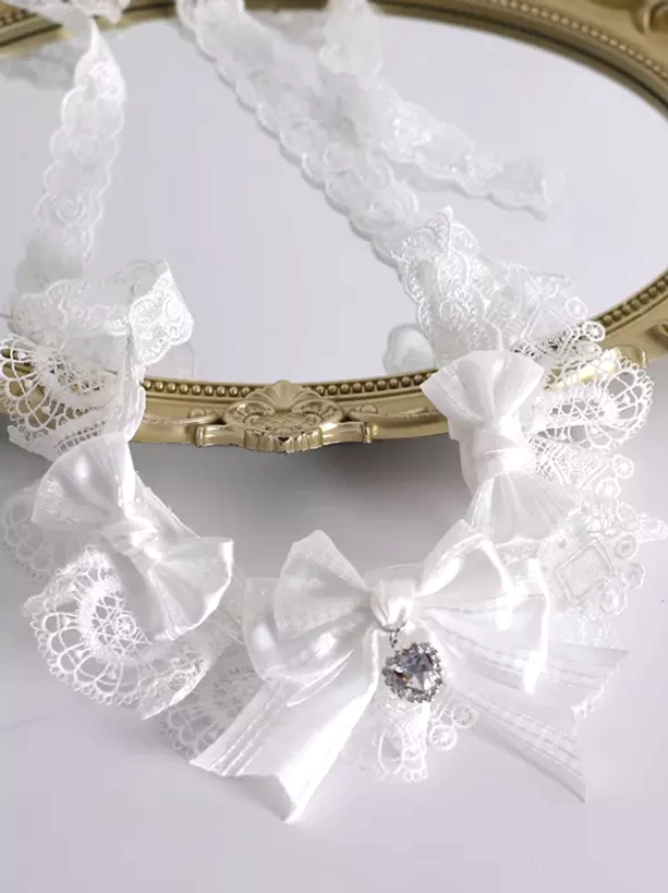White lace bow choker with adjustable tie straps and heart crystal charm flat lay on vintage gold mirror lolita neckwear