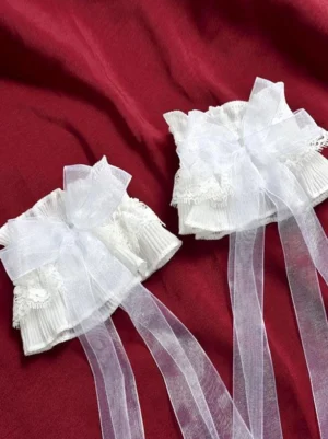 White lace oversleeves with ruffled lace cuff and organza bow on red fabric background, flat lay photography showing delicate Rococo sweet lolita arm accessories with long sheer ribbon tails