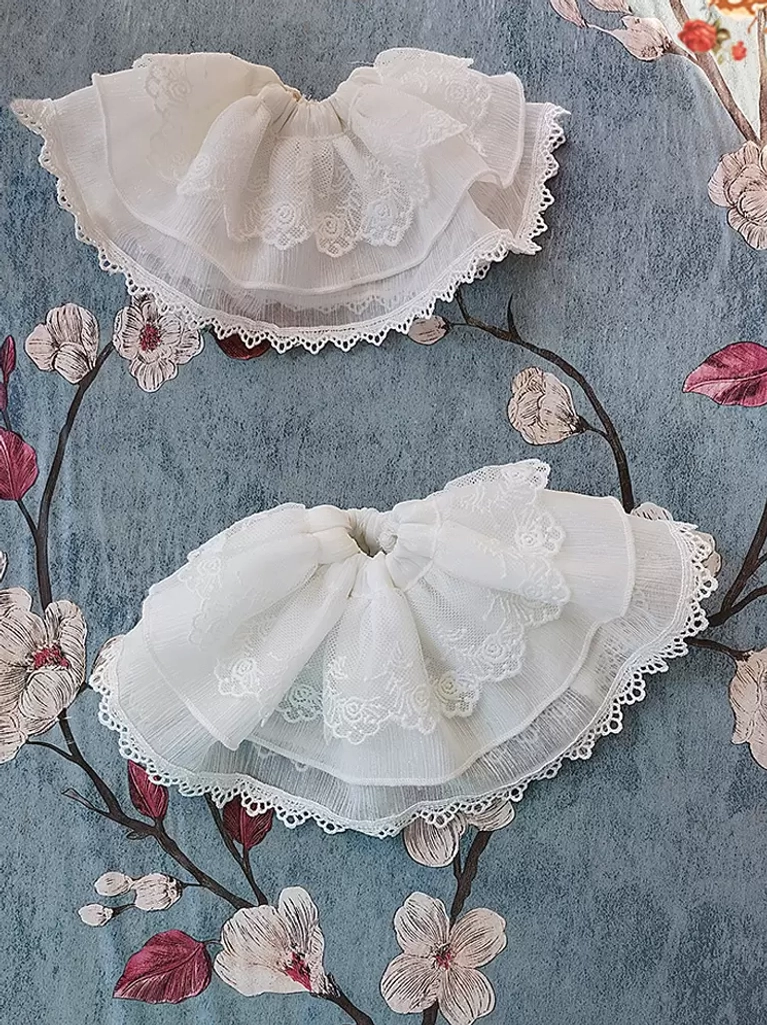 Flat lay of white ruffled lace lolita accessories double-layer pleated mesh with embroidered lace trims on floral fabric background