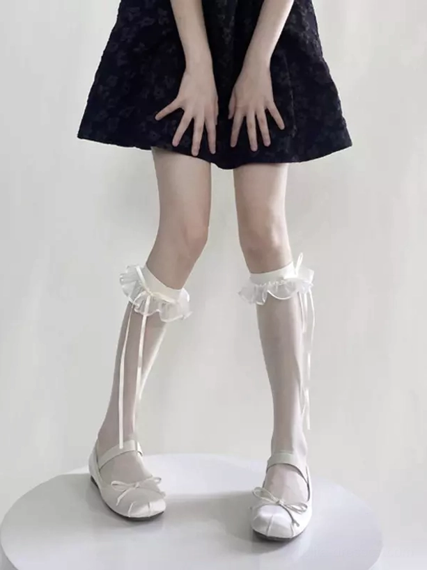 Front full view of white ruffled ribbon calf socks featuring delicate sheer fabric, frilled edge trim, and extended satin ribbon ties on standing model in black mini dress