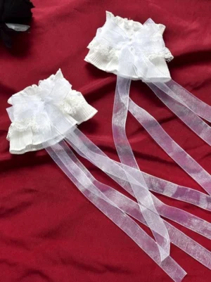 Detailed top-down view of white lolita lace oversleeves featuring ruffled lace construction and flowing ribbon tails against red fabric backdrop, showcasing sweet lolita arm accessory design