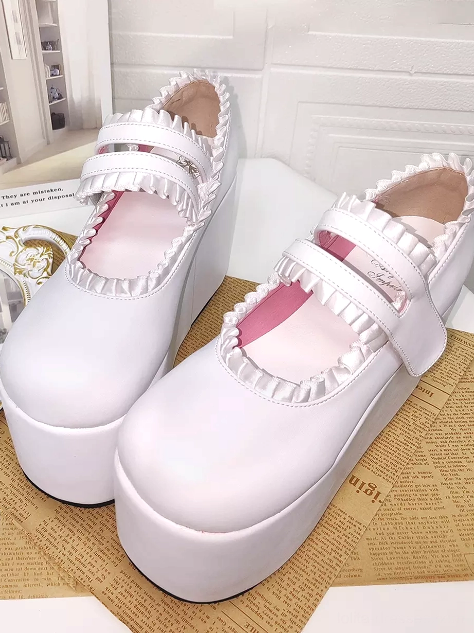 Pair of white sweet lolita platform shoes front close-up view with double velcro straps, ruffled collar trim, pink inner lining, styled with vintage decor and newspaper background