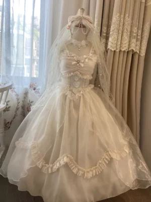 White sleeveless sweet lolita wedding dress with ruffled skirt, attached veil, and pearl embellishments, full front view on dress form with floral background