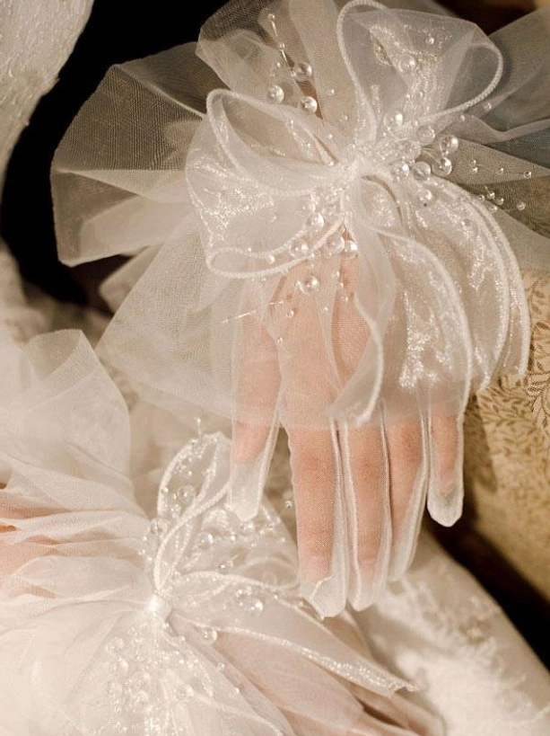 white mesh bow gloves with rhinestone beads worn on model hands paired with white lace wedding dress close-up top view