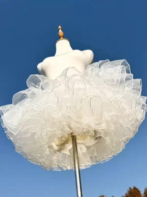 White ultra-short lolita petticoat with 4-layer ruffled organza tiers displayed in outdoor low-angle front view with blue sky background, showcasing fluffy puff silhouette perfect for sweet and casual lolita fashion