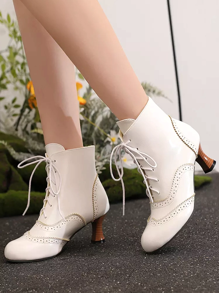 White vintage lace-up ankle boots with brogue perforations and brown wooden chunky heel, shown from side and rear-side angle in outdoor floral setting, displaying delicate decorative details perfect for Lolita coordinates
