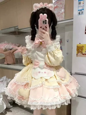 Yellow sweet cat print lolita dress with pink gradient ruffled skirt, long lantern sleeves, lace trims, and bunny chest ornament worn by model with pink cat ear headband
