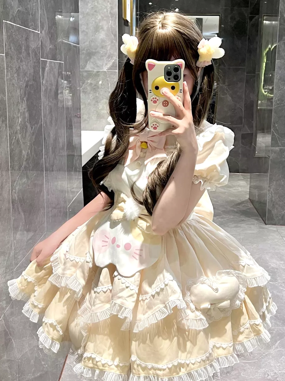 Yellow sweet lolita cat dress front view with beige color ruffled skirt, cat face decoration and plush cat ornament, model making peace sign in marble indoor scene